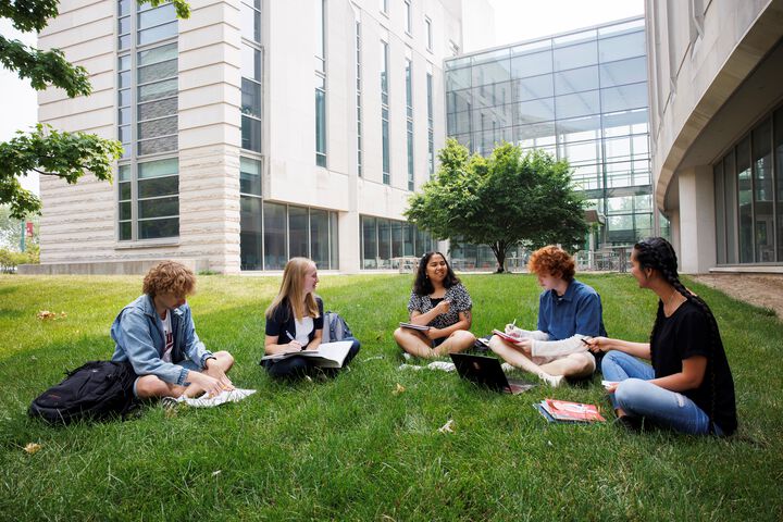 Students sit on the grass outside of the Hamilton Lugar building.